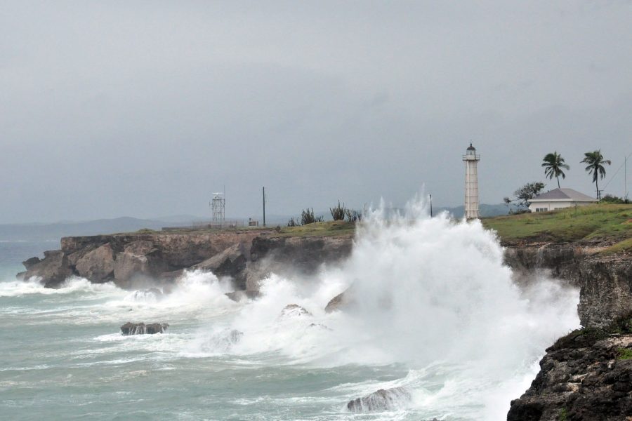 An image of a wave breaking on a rocky shore on the Cuban coast with a light house and other structures standing on the shore.